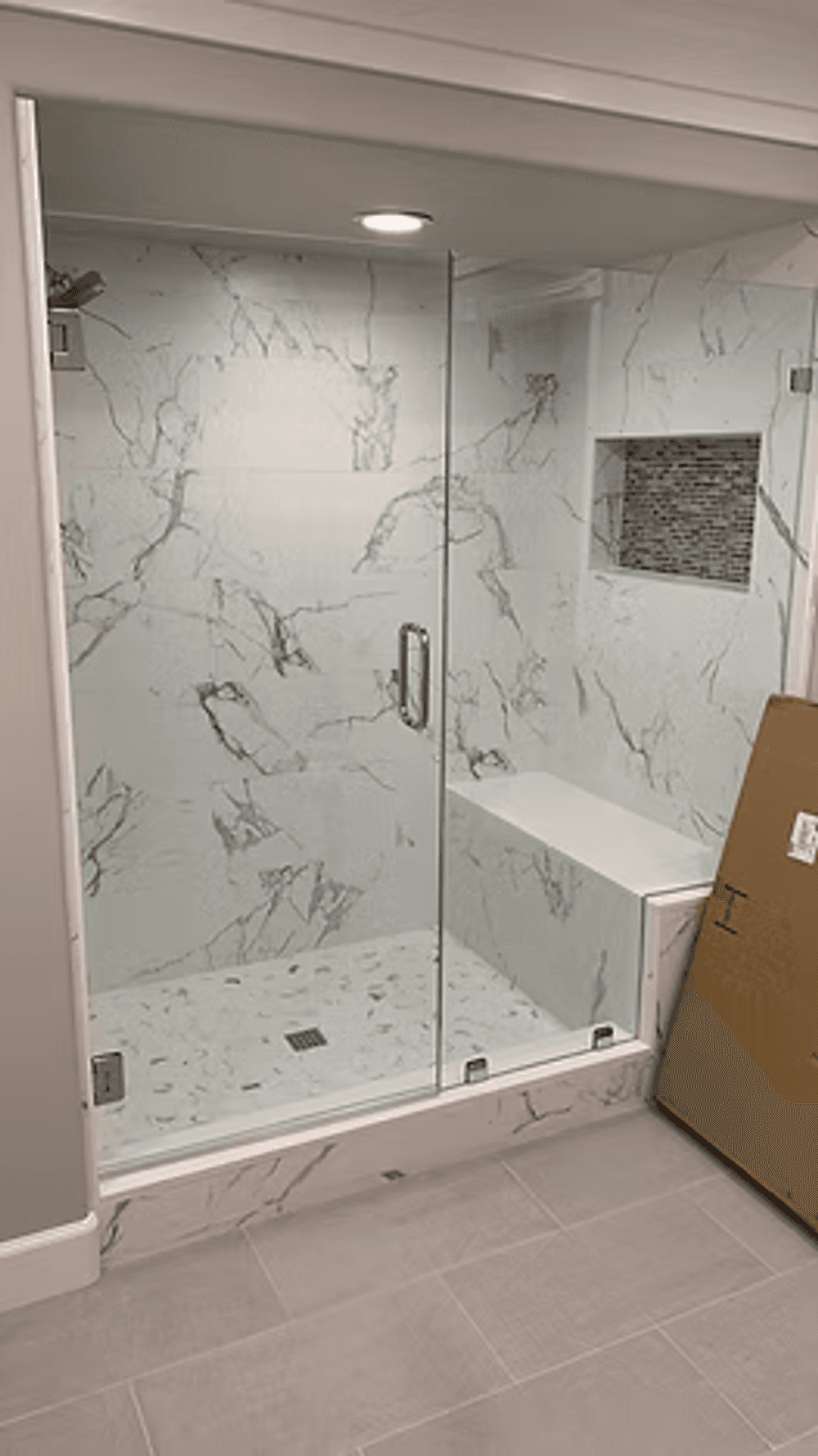 Modern glass shower enclosure with marble walls, built-in bench, and stylish tile accents.