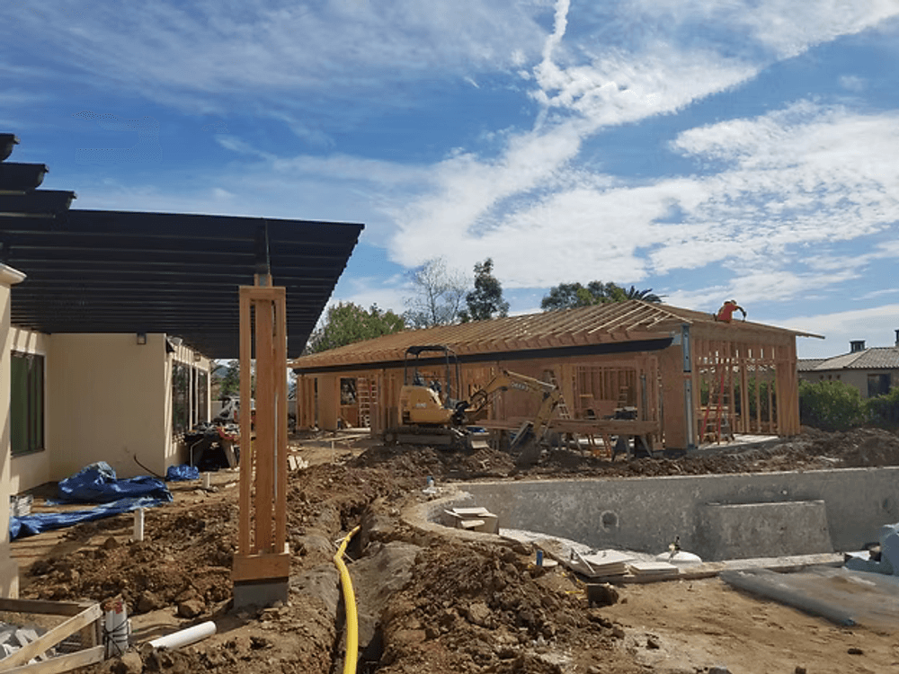 Construction site with framing and machinery under a blue sky, showcasing ongoing building work.
